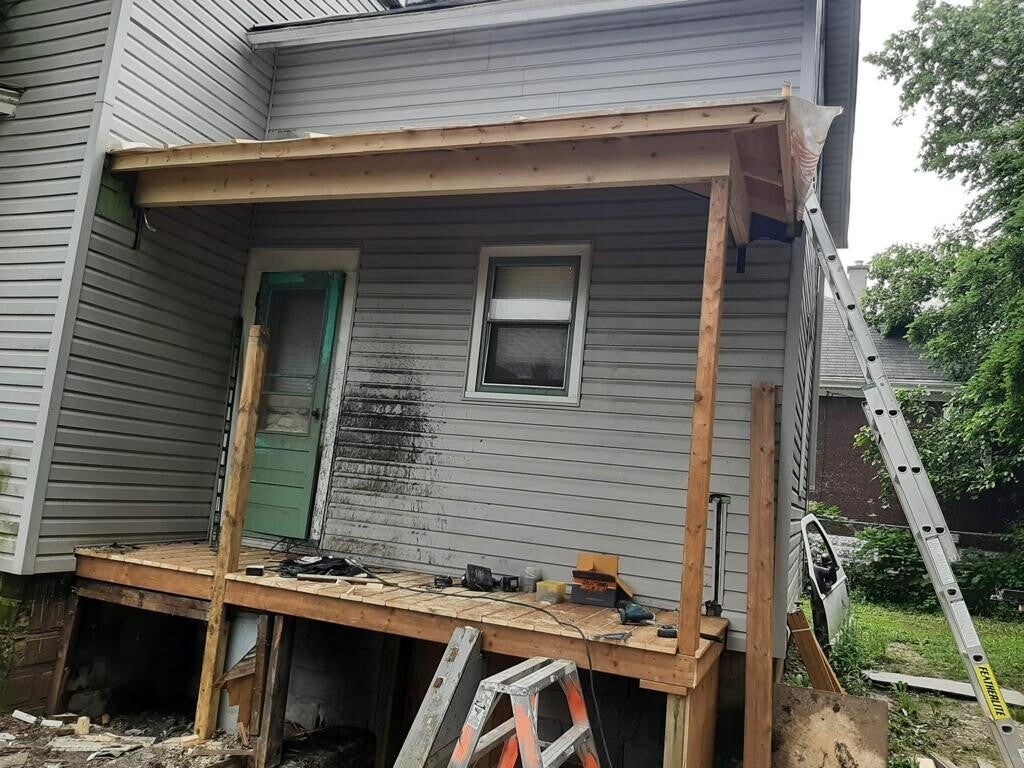 Timber posts and beams supporting the framed porch roof above a rebuilt wood platform.